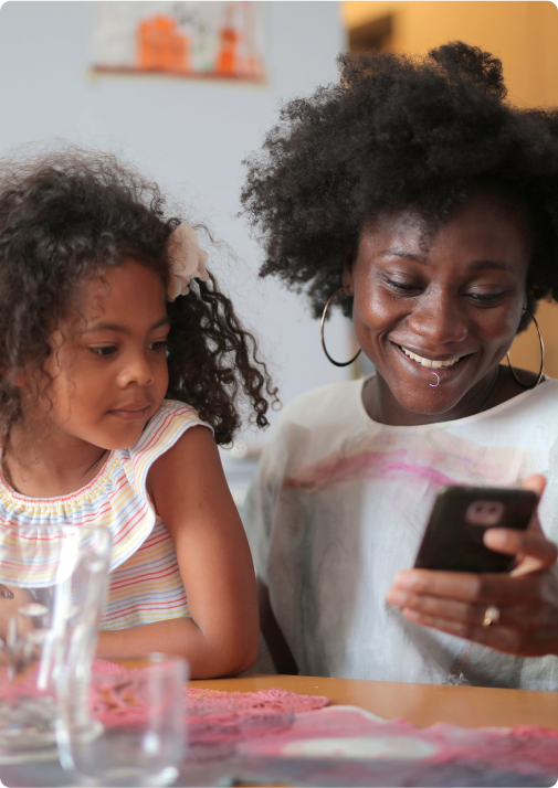 Mother and daughter at kitchen table smiling at phone