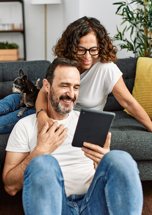 Woman sitting on couch with small dog and looking at tablet with husband