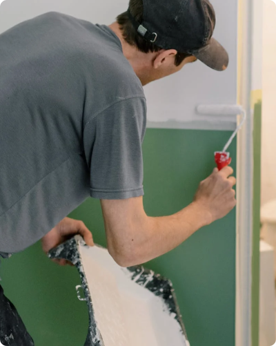 Painter coating wall with white paint above trim